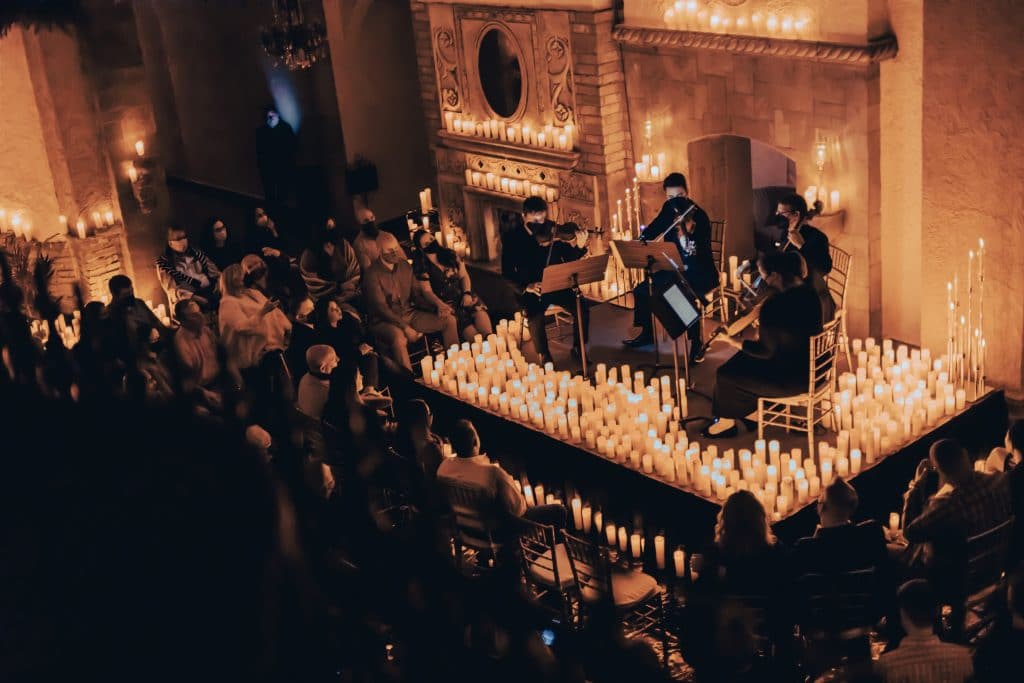 A string quartet is performing on a stage covered in candles with an audience wrapped around the stage.