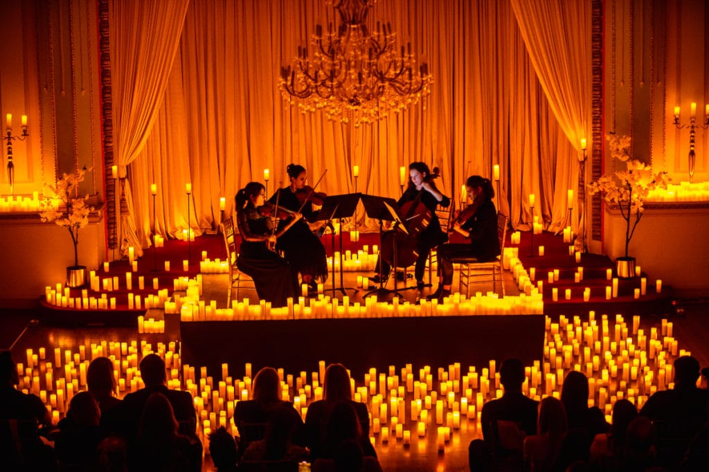 A string quartet performing on a stage covered in candles and an orange-coloured curtain forming the background.